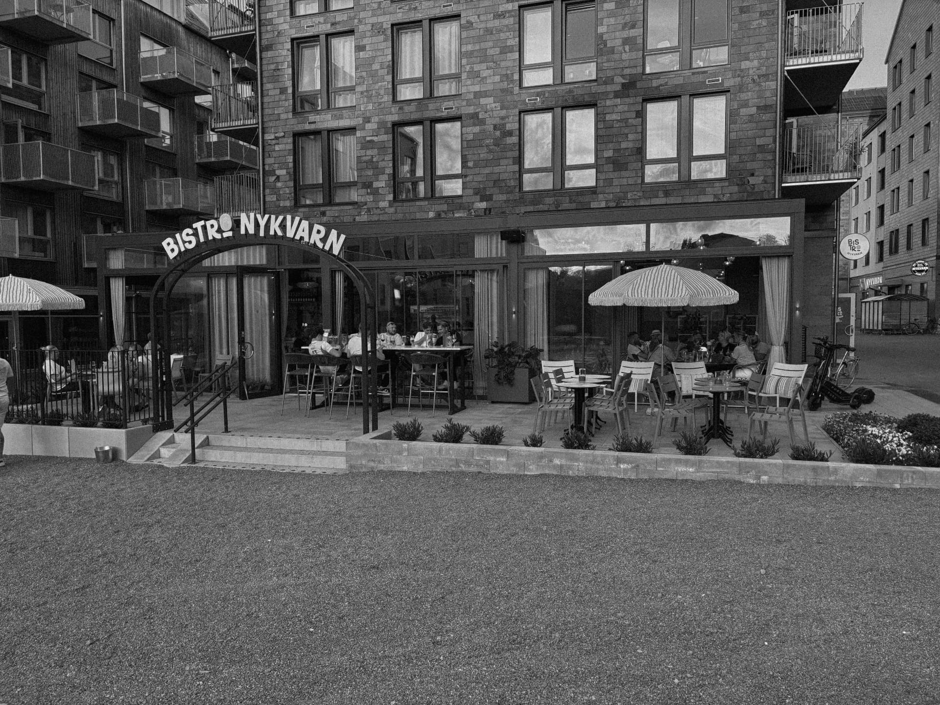 Bistro Nykvarns fasad med skylt, uteservering och parasoller i svartvitt